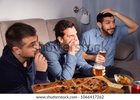 Worried concentrated serious men watching sporting match on tv with beer and pizza at home