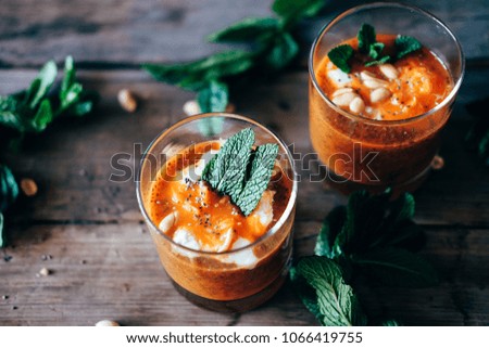 Cold and spicy red carrot cream soup with peanuts, chia seeds and mint served in glass cups.