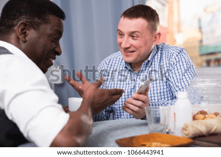 Smiling man meeting with African friend at home, looking at phone and discussing