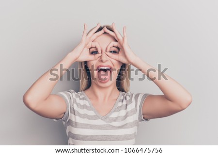 Portrait of crazy, pretty, charming, stylish, creative girl showing tongue out and binoculars on eyes with fingers 