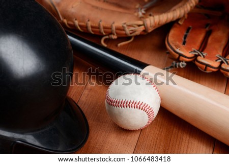 Baseball, helmet and bat on wooden table. Catcher and pitcher's gloves in blurred background.