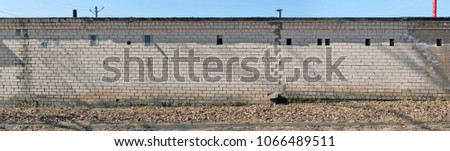 The reverse long wall of cooperative public garages is made of white silicate bricks. Ventilation holes are covered with iron flaps. Papnoramic collage from several outdoor sunny day photos