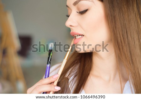 Portrait of talented young woman painting picture in art studio with inspiration