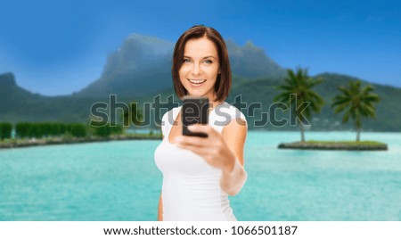 travel, tourism, summer holidays and vacation concept - happy young woman taking selfie by smartphone at touristic resort over bora bora island beach background