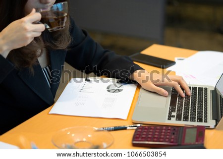 Working woman drinking coffee during working with her laptop with calculator, pen, notebook and paper sheet on her desk.