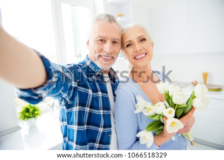 Self portrait of lovely cheerful stylish modern attractive couple, man shooting selfie on front camera, woman holding bouquet of tulips, having rest, relax, enjoying spring, morning