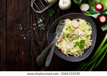Diet, concept of vegetarian food. Summer salad with fresh cabbage and radish dressed with olive oil on a wooden table. Healthy proper nutrition. Top view flat lay background.
