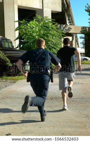 Policeman chasing after running away suspect man Royalty-Free Stock Photo #1066532603