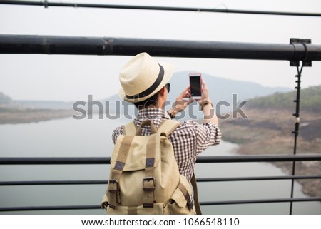 Young man tourist using phone and selfie on the rope bridge with blurry nature background.