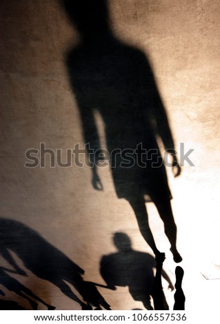 Blurry silhouette shadow of one young woman and young family with children holding hands while walking behind her in sepia black and white in summer