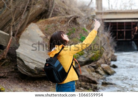 A girl in glasses travels near a mountain stream with a telephone.