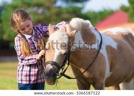 Beautiful little blonde girl embraces horse pony. She has happy fun smiling face, pretty eyes, plaid shirt. Kids and animals portrait. Creative amazing concept. Happy couple friends.