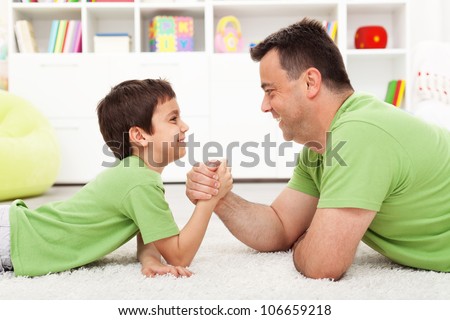 Father and son arm wrestling at home - childhood and parenting