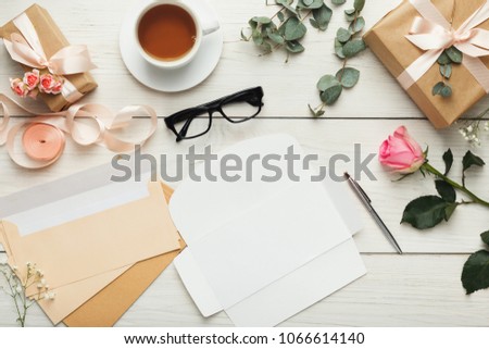 Wedding invitations and craft envelopes on white wooden background. Top view on paper cards, rings and pink roses bouquet, copy space. Memmorable date organization concept