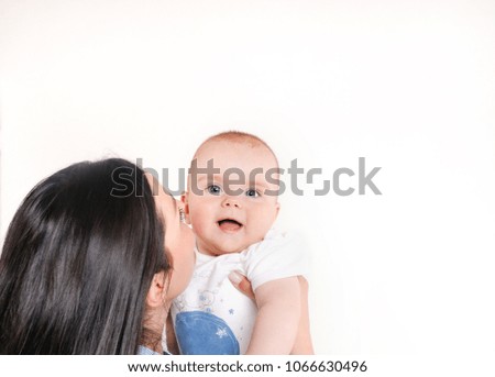 Mum kissing her son on a white background. Newborn looking at the camera. Happy motherhood concept