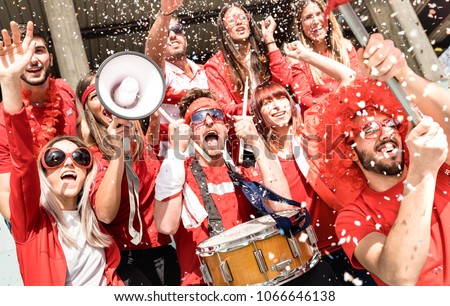 Young football supporter fans cheering with flag and confetti watching soccer match at stadium - Friends people group with red t-shirts having excited fun on sport world championship concept Royalty-Free Stock Photo #1066646138