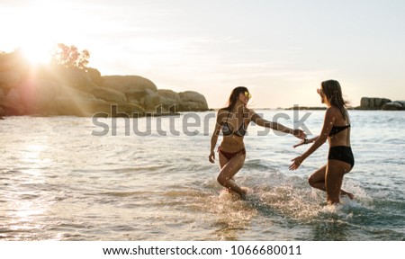 Two women playing and walking in sea water. Female friends having fun on beach vacation.