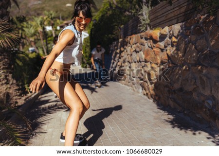 Attractive young woman skateboarding on sea walk front during a summer vacation with friends in background. Young people doing skating by the beach.