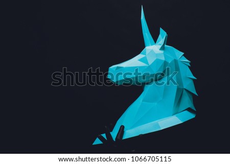 Unicorn head paper on black background. Hands in black gloves hold a turquoise Unicorn. Copy space