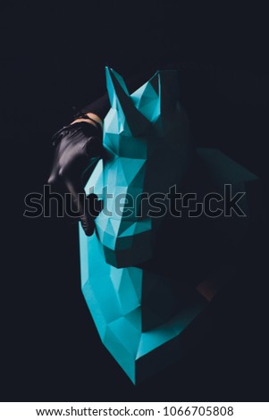 Unicorn head paper on black background. Hands in black gloves hold a turquoise Unicorn. Copy space