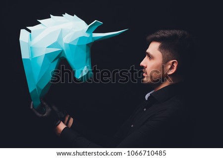 Man in black gloves holds origami. Unicorn turquoise head paper isolated on black background. Copy space. Model mythical creature. Male