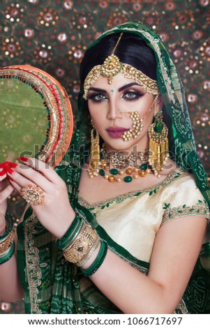 Beautiful Muslim Woman face portrait with bindis and paint.  Close up of beauty indian woman with perfect makeup and big green eyes. Traditional Maang Tikka , Nath,  Nose Pin