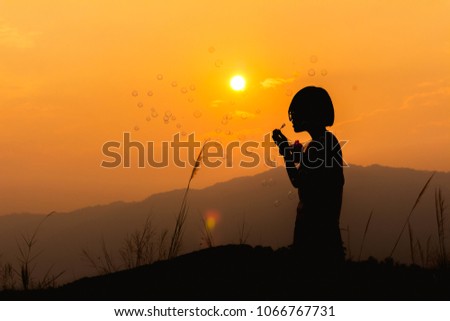 Silhouette little girl playing with bubble wand on mountain at sunset background