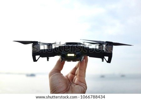 Close up of man hand holding a mini drone facing ocean, ready to be released in the sky.