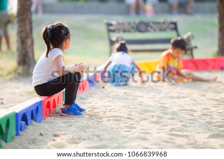 Little girl sitting lonely watching friends play at the playground.The feeling was overlooked by other people. Royalty-Free Stock Photo #1066839968