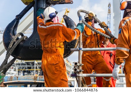 Offshore workers installing big sling onto crane block in preparation of heavy lifting of structure frame from a construction barge to oil platform Royalty-Free Stock Photo #1066844876