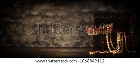 Image of mysterious opened old wooden treasure chest and queen/king crown with red Rubies stones. fantasy medieval period. Selective focus. banner format