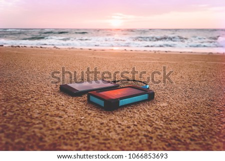 Powerbank in the sand on background of the rising sun in the cloudy sky and blue sea. Alternative energy source. battery is charged by solar energy. Charging mobile devices in the wild. island beach