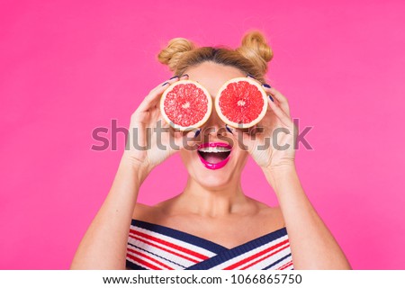 Beauty Model Girl takes Juicy Grapefruit. Beautiful Joyful young girl, funny blonde hairstyle and pink makeup.Holding Orange Slices and laughing, emotions. Royalty-Free Stock Photo #1066865750
