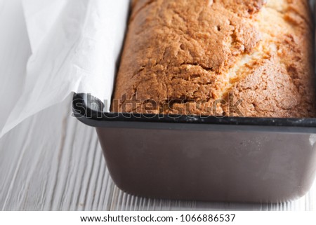 Banana bread in a pan with white parchment paper on a white wooden table. Minimal food photography styling. Vertical, flat lay. Close up macro. Texture cracks Royalty-Free Stock Photo #1066886537