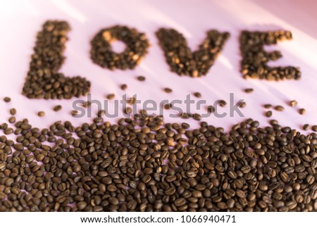 Spilled roasted coffee beans on a pink background with a love inscription.