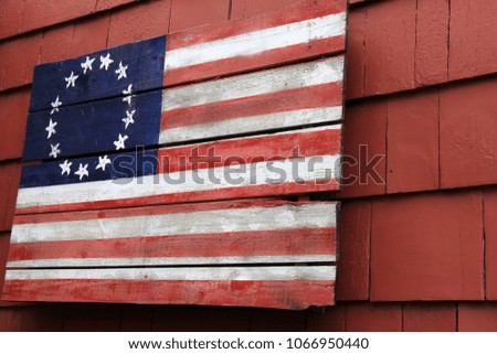 Old worn wood decoration painted with colors of the flag, hanging on exterior wall of building.
