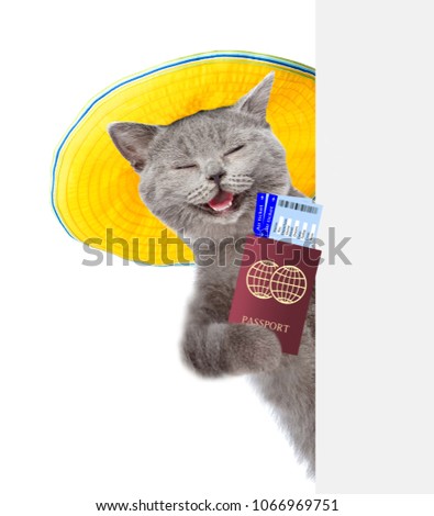 Happy cat with summer hat holds airline tickets and passport behind white banner. isolated on white background