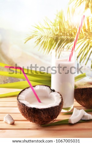 Coconut drink in glass with fruit on wooden table on tropical beach background. Alternative milk concept. Front view. Vertical composition.