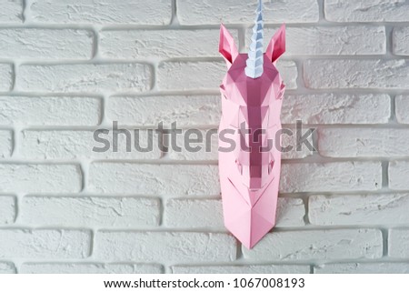 pink unicorn's head is hanging on white brick wall. Horse has intresting geometrical shape and straight lines. Original decoration for modern design.