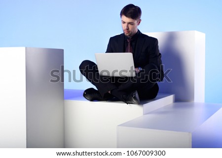 businessman using laptop while sitting on white block isolated on white
