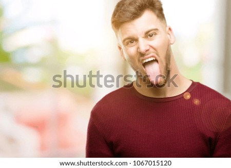 Handsome young man sticking out tongue at camera at sign of disobedience, protest and disrespect