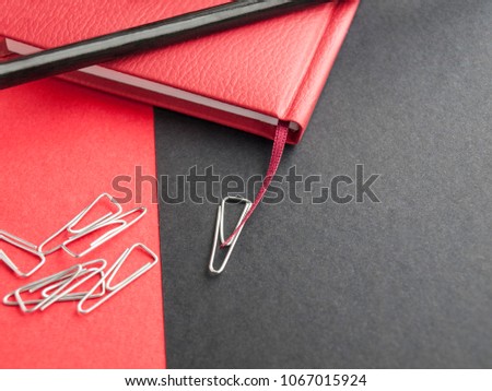 Office supplies: a red notepad, pencil and paper clips on a black background. Top view. Copy space.