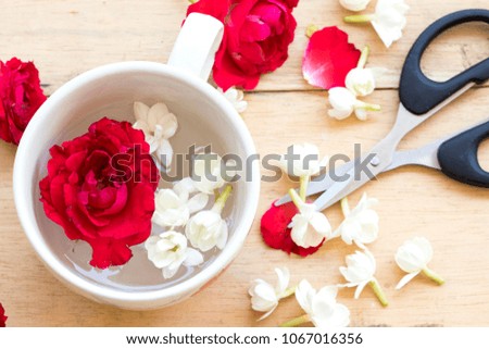 red rose and jasmine flowers float water in cup with scissors on background wooden