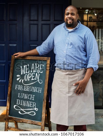 A cheerful business owner standing with open blackboard