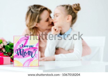 mother hugging daughter with postcard on foreground, happy mothers day concept