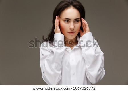 Beautiful girl in a white shirt shows emotions - headache. On a light background.