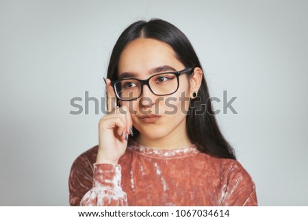 beautiful asian girl has a great idea, wears glasses and pink sweater, studio photo on background