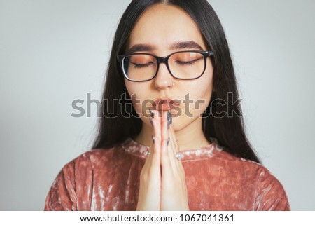 beautiful asian girl praying or meditating, wearing glasses and pink sweater, studio photo on background