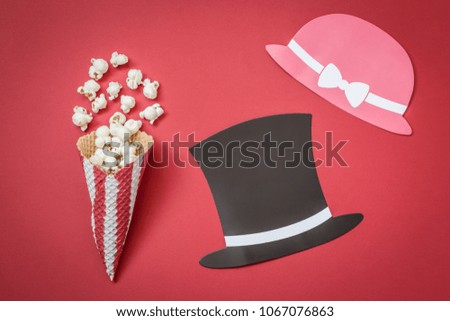 Flat lay of cone and popcorn with man and woman paper prop hats on red background minimal movie theater concept
