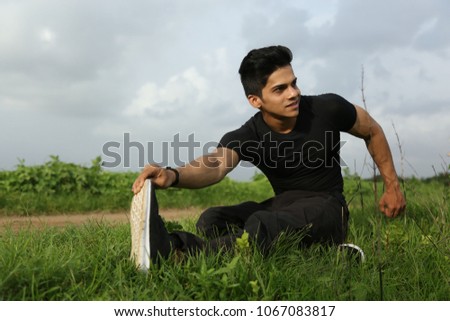 Fit young man doing stretching exercise outdoors at park Royalty-Free Stock Photo #1067083817